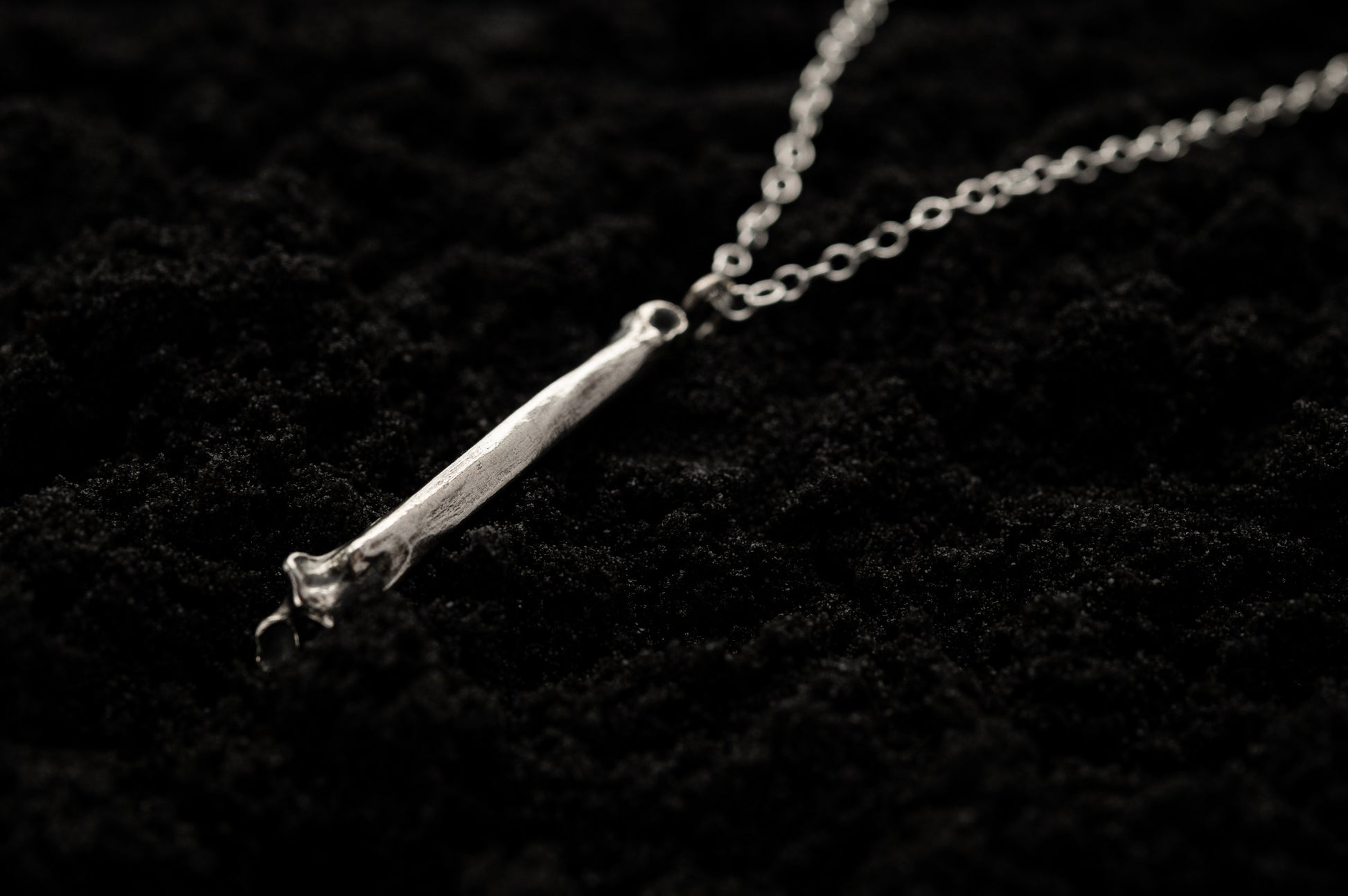 Silver Bone Necklace Laying on Black Sand